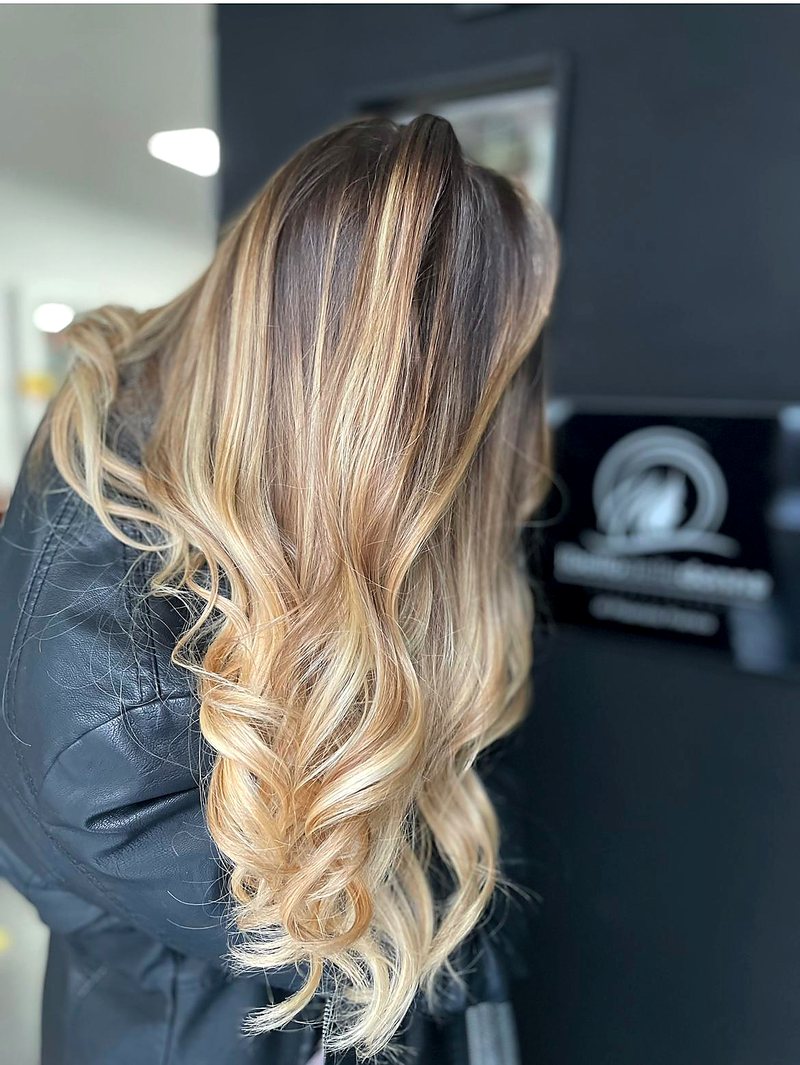 Balayage biondo su base scura, onde lunghe, fotografato nel salone