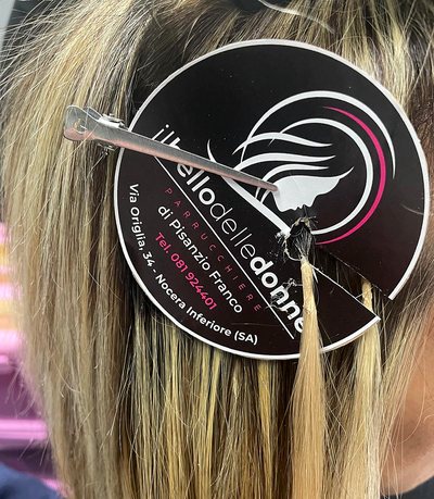 Ciocca di extension appoggiata su capelli biondi, con la targhetta del salone