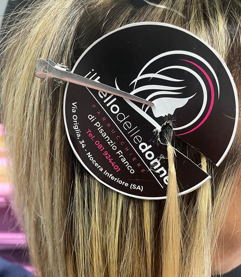 Ciocca di extension appoggiata su capelli biondi, con la targhetta del salone