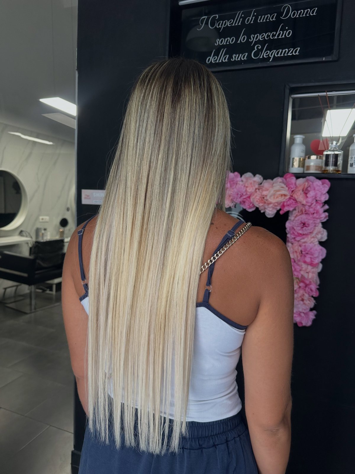 Capelli biondi lunghissimi con radice sfumata, ripresi di spalle nel salone Il Bello delle Donne, davanti alla parete di fiori rosa
