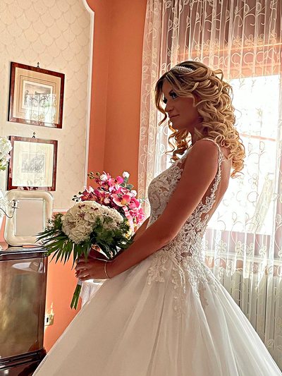 Sposa con acconciatura riccia semiraccolta, in controluce davanti alla finestra