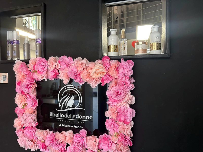 La targa del salone Il Bello delle Donne incorniciata dai fiori rosa, sulla parete scura